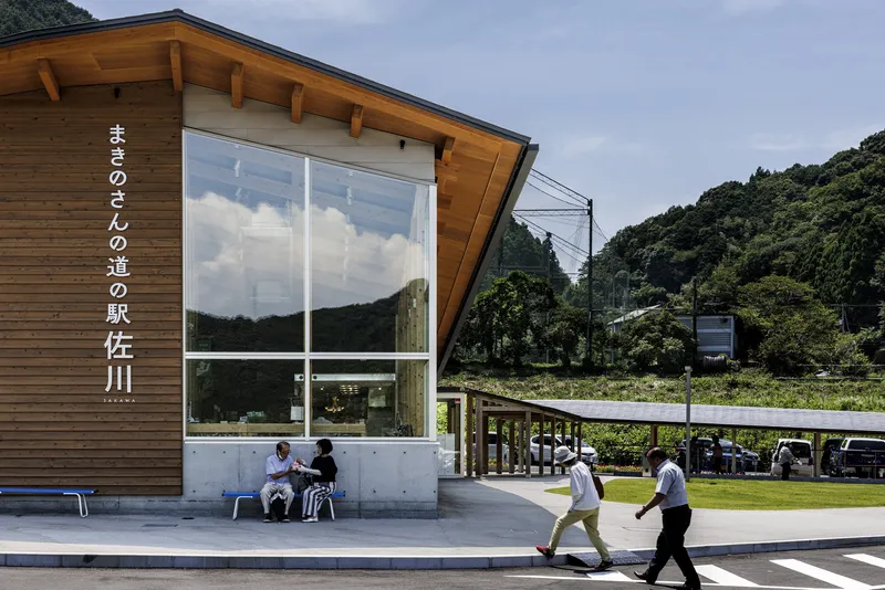 Angled timber-clad entrance pavilion with large glazed corner and people sitting beneath overhang