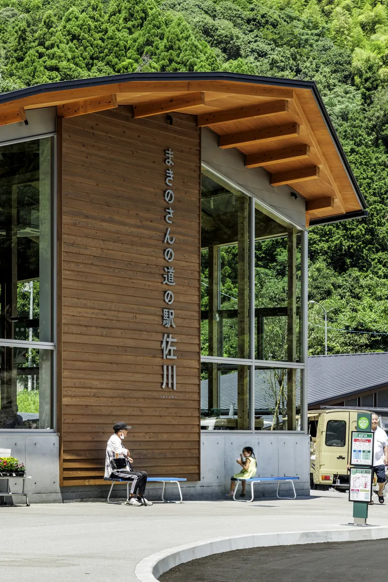 Timber entrance volume with projecting roof beams and glazed walls while visitors occupy benches below