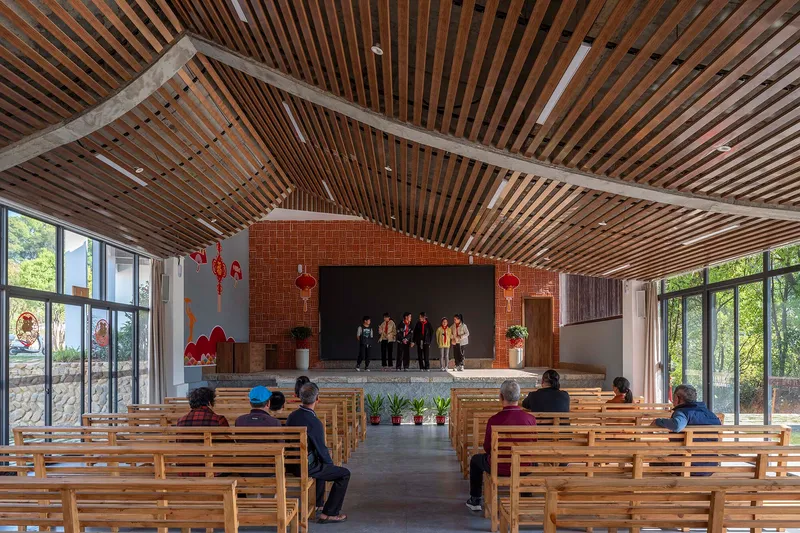 Interior hall with timber slat ceiling, wooden benches and a raised stage platform with brick chimney