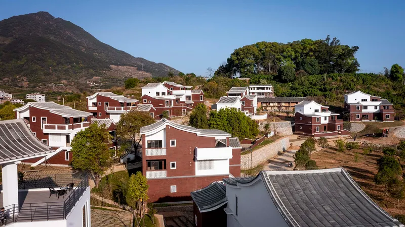 Housing cluster on sloped terrain with red brick and white volumes under curved tile roofs with mountains behind