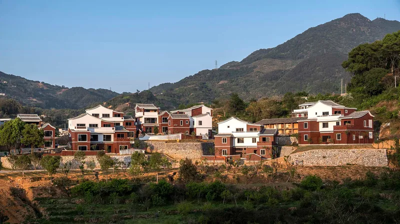 Cluster of red brick and white stucco houses on a hillside beneath a forested mountain