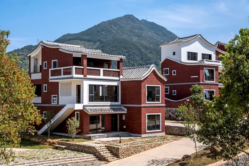 Front facade of clustered red brick and white volumes with curved tile roofs and terraced stone walls