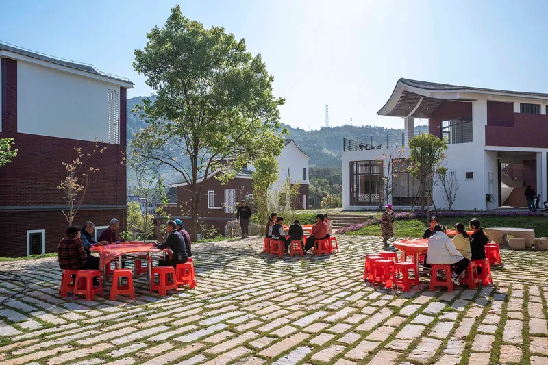 Residents seated at red tables and stools on a permeable paving grid in midday sun