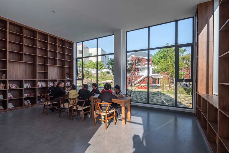 Library reading room with timber shelving and a group seated at tables by floor-to-ceiling windows