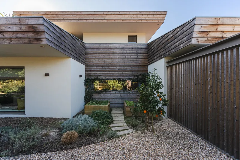 Courtyard entry with weathered timber cladding and gravel path leading between planted beds at dusk