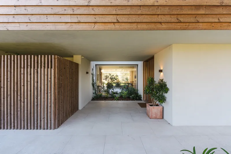 Covered entry passage with timber slat wall and exposed wood ceiling framing an interior courtyard view