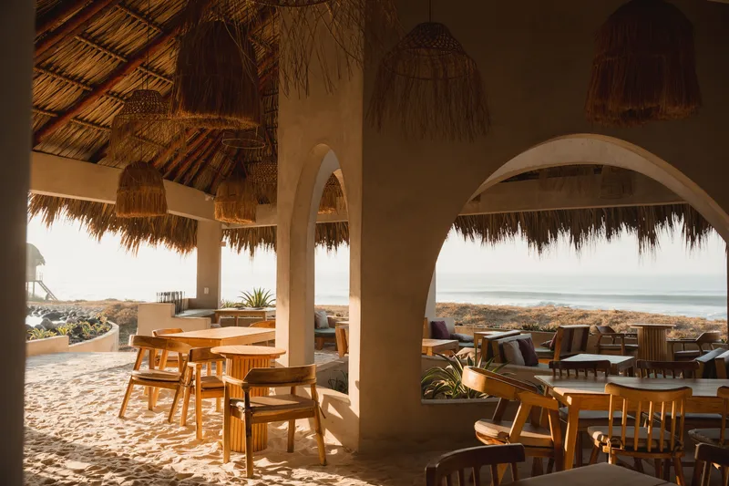Interior view through arched thatch-trimmed openings to the dining terrace and coastal landscape beyond