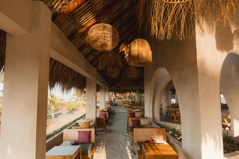 Interior corridor with thatch roof, woven pendant lights and arched openings leading to seating areas