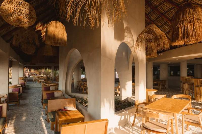 View through the arched interior colonnade with thatched roof and sunlight streaming across the polished floor