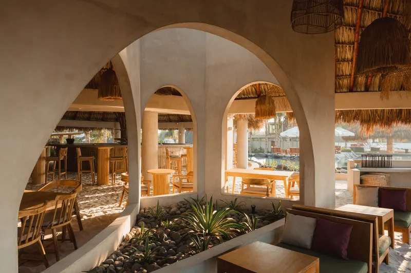 White stucco arches framing a planted bed with agave and a dining area with thatched pendants