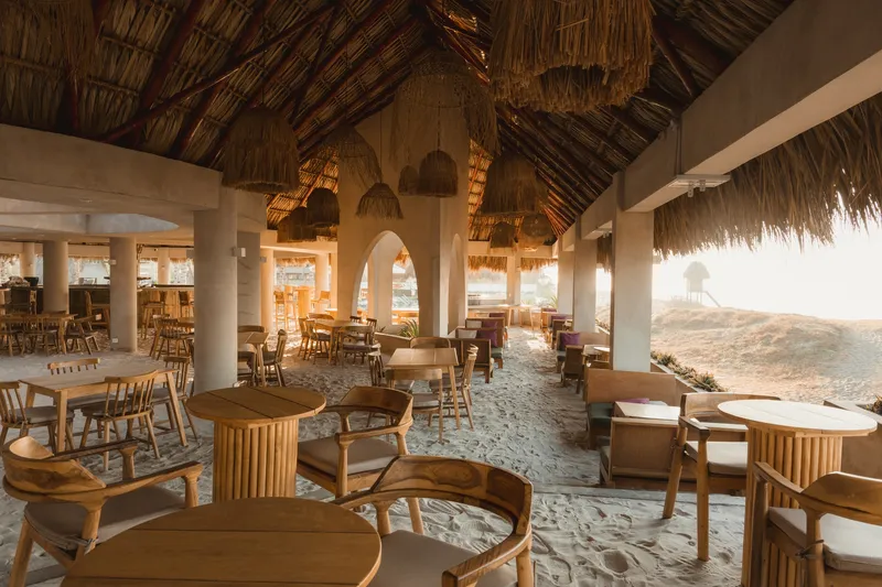 Open-air dining pavilion with thatched roof, white columns and sand floor overlooking the ocean