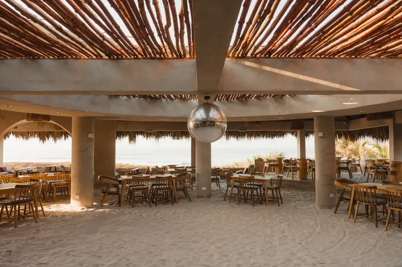 Dining area with exposed timber ceiling beams and a mirrored disco ball suspended from a concrete beam