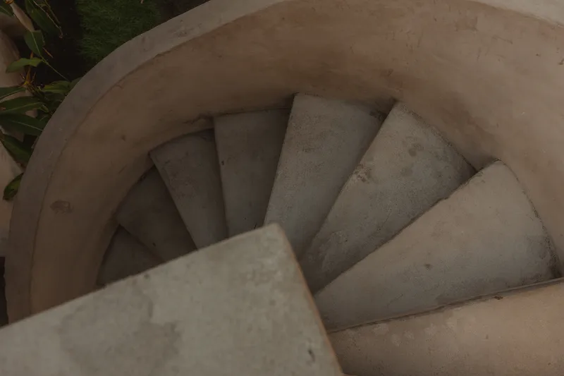 Top-down view of a circular concrete staircase descending with palm foliage visible at the edge