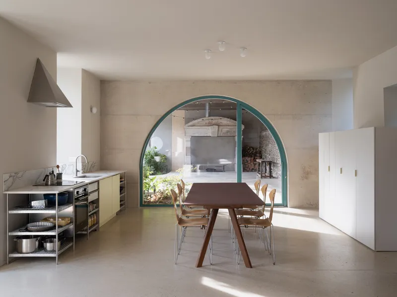 Open kitchen and dining area viewed through large arched doorway with teal frame and stone wall beyond