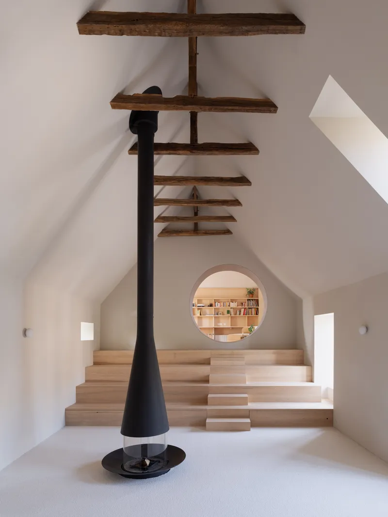 Wooden staircase with black steel woodstove and circular viewing portal framed by white plastered walls