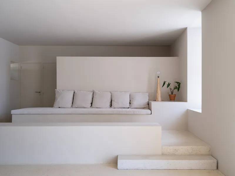 Built-in seating nook with white cushions and stone steps ascending under a low ceiling
