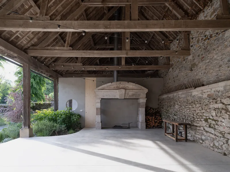 Exposed timber roof trusses over stone fireplace with original masonry walls and stacked firewood