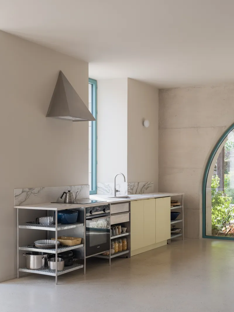 Kitchen counter with marble backsplash, open metal shelving, and conical metal range hood under soft daylight