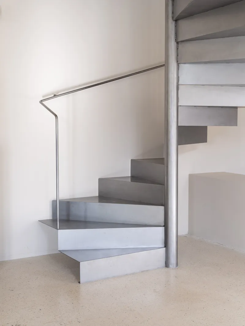 Close view of grey metal spiral staircase treads with slim tubular railing against terrazzo floor