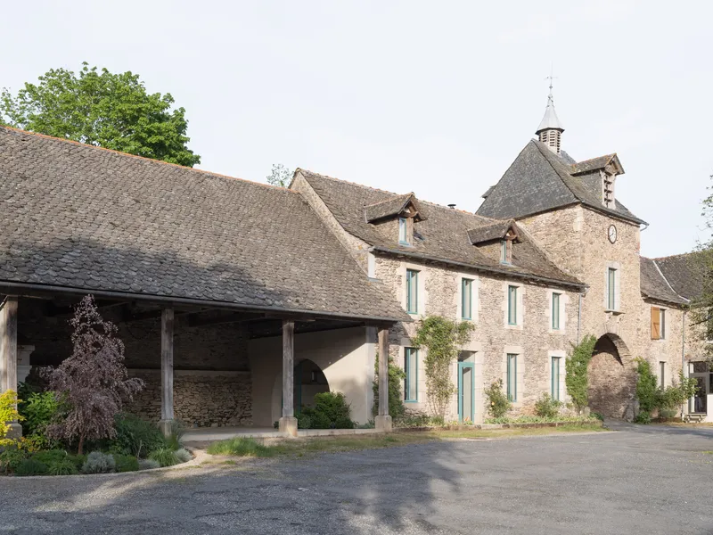 Street view of the stone farmhouse complex with timber woodshed and bell tower under overcast skies