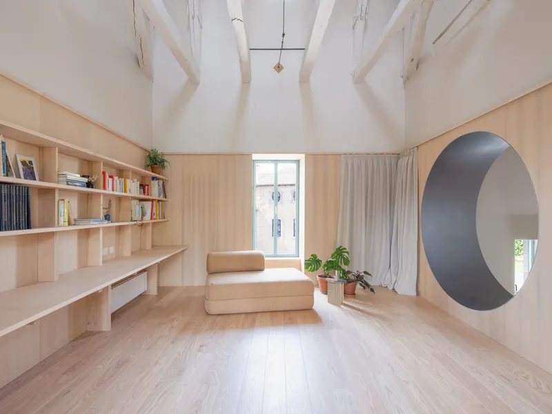 Interior room with exposed timber rafters, plywood built-in shelving and circular portal opening in soft daylight