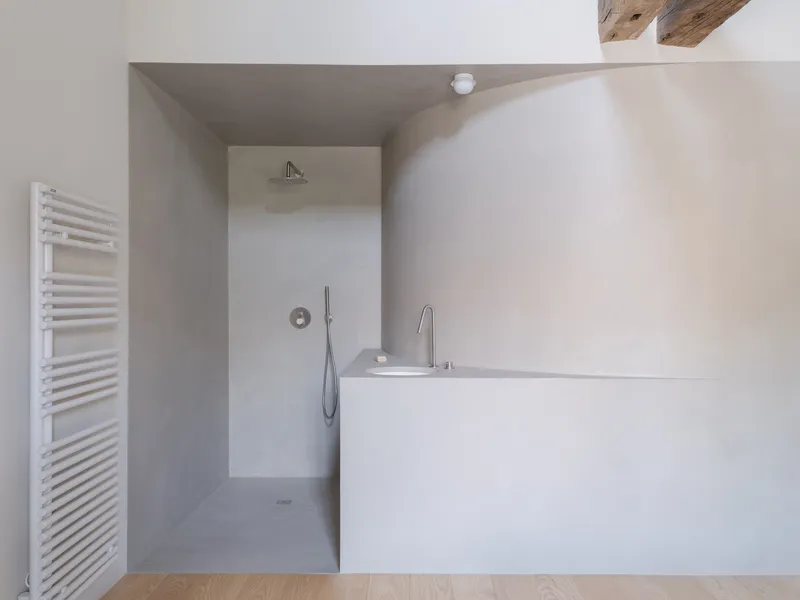Bathroom with tadelakt-finished bathtub and walk-in shower alcove under exposed timber beams