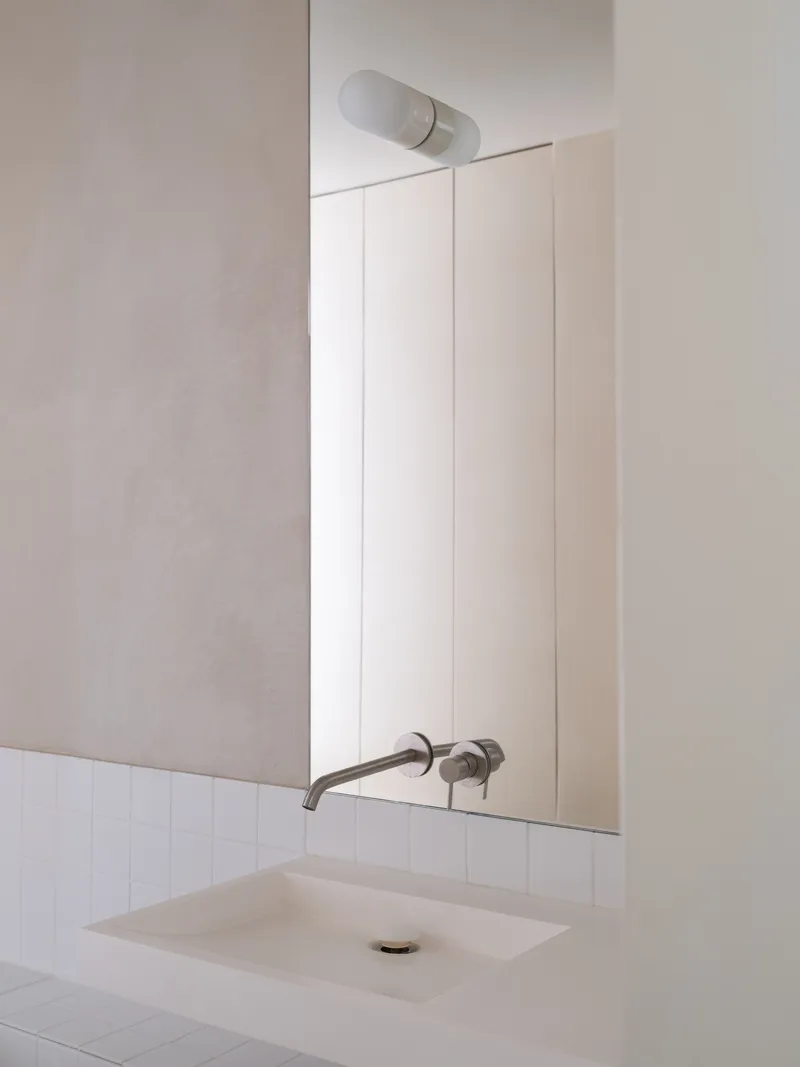 Bathroom vanity with undermount sink and wall-mounted taps below a frameless mirror and cylindrical sconce