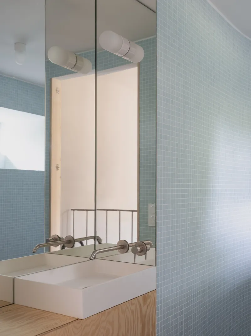 Bathroom mirror reflecting pale blue mosaic tile wall and handrail with timber vanity below