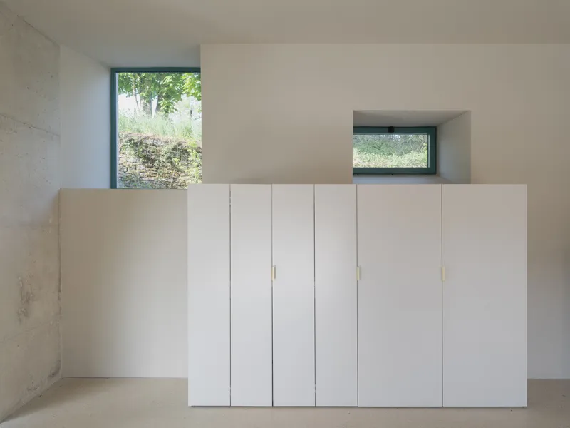 White storage cabinet with brass pulls beneath deep window looking onto garden with stone wall