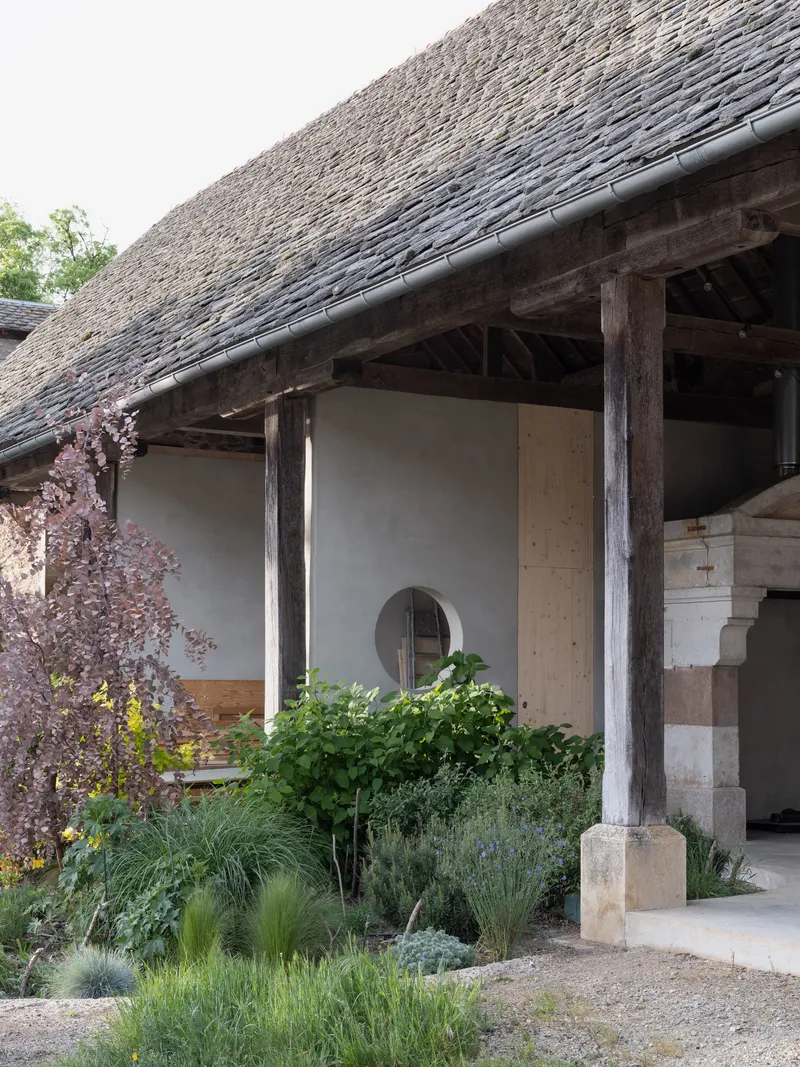 Covered porch with weathered timber columns and thatch roof overlooking a planted courtyard with grasses and shrubs