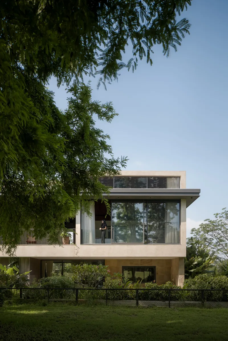Three-story facade with stacked terraces and glazing framed by overhanging tree branches