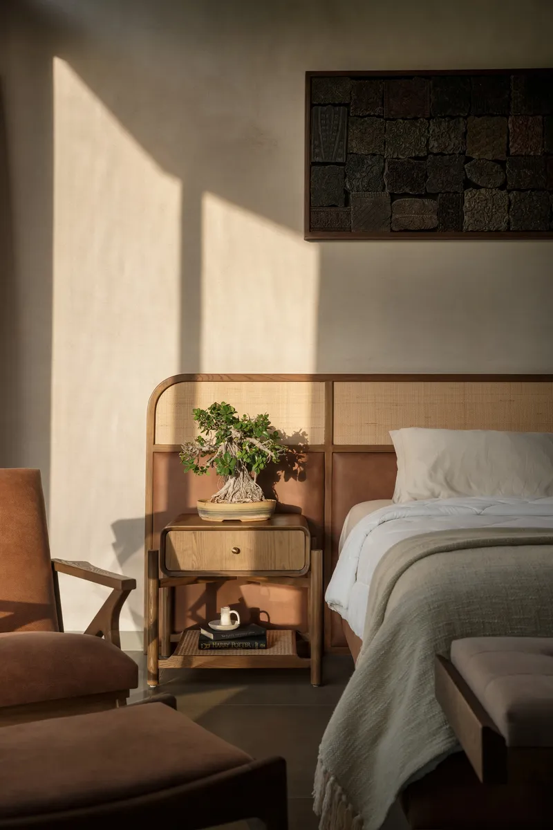 Bedroom nightstand in warm afternoon sunlight with bonsai tree and cane-panel detailing below artwork