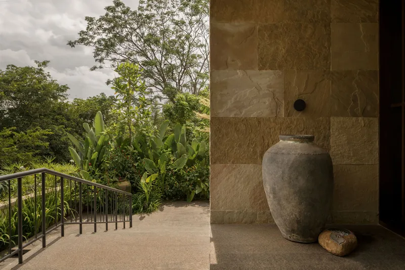 Entry threshold with stone-clad wall, ceramic urn, and metal railing leading to planted hillside