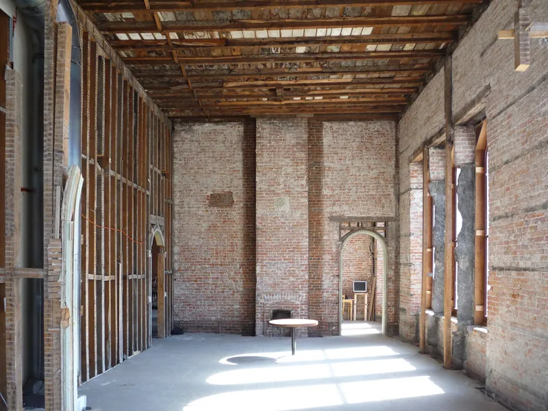 Exposed brick interior room with timber beamed ceiling and arched doorway allowing sunlight through
