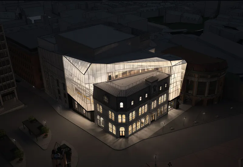 Aerial view of a glowing glass addition wrapping a historic masonry corner building at dusk