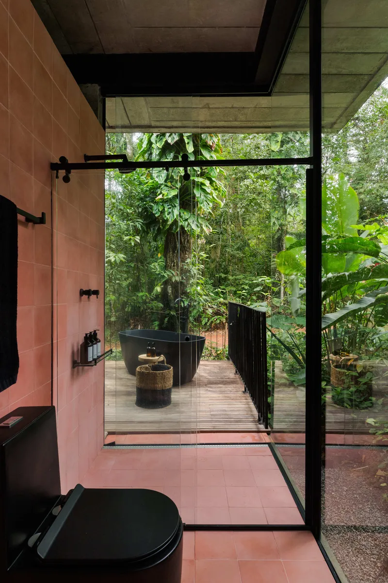 Bathroom with terracotta tile floor and walls leading to timber deck terrace surrounded by jungle canopy