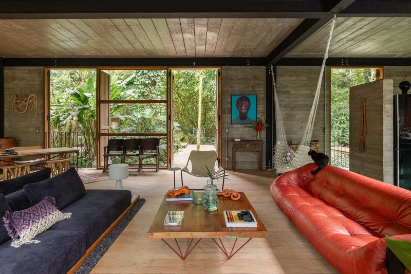 Living room with board-formed concrete walls, exposed ceiling beams, and floor-to-ceiling windows facing vegetation