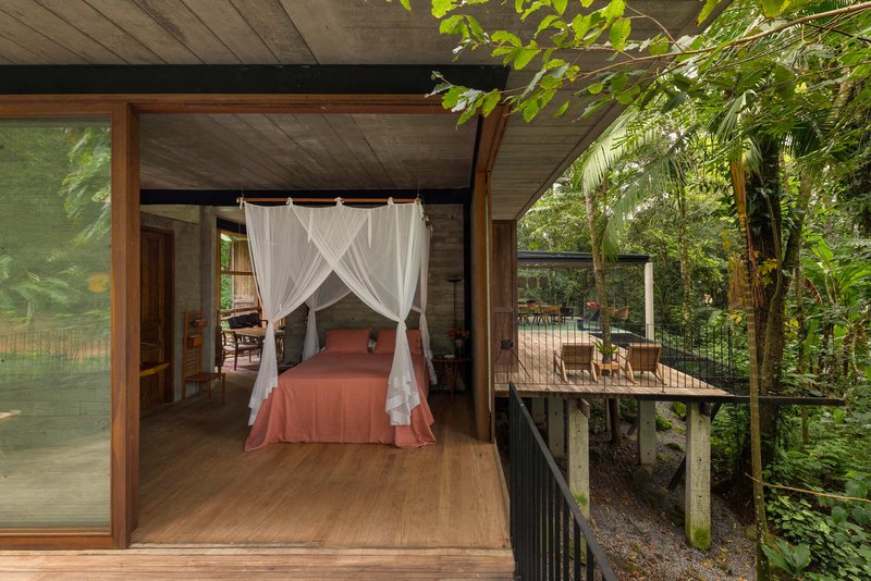 Interior bedroom with canopy bed opening to a timber deck surrounded by jungle foliage