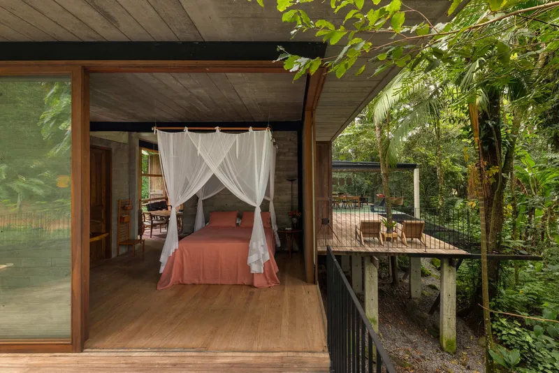 Interior bedroom with canopy bed opening to a timber deck surrounded by jungle foliage