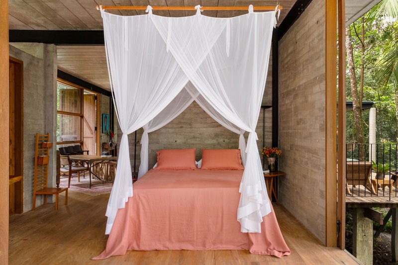 Bedroom with white canopy netting over bed and timber-planked ceiling opening to surrounding forest