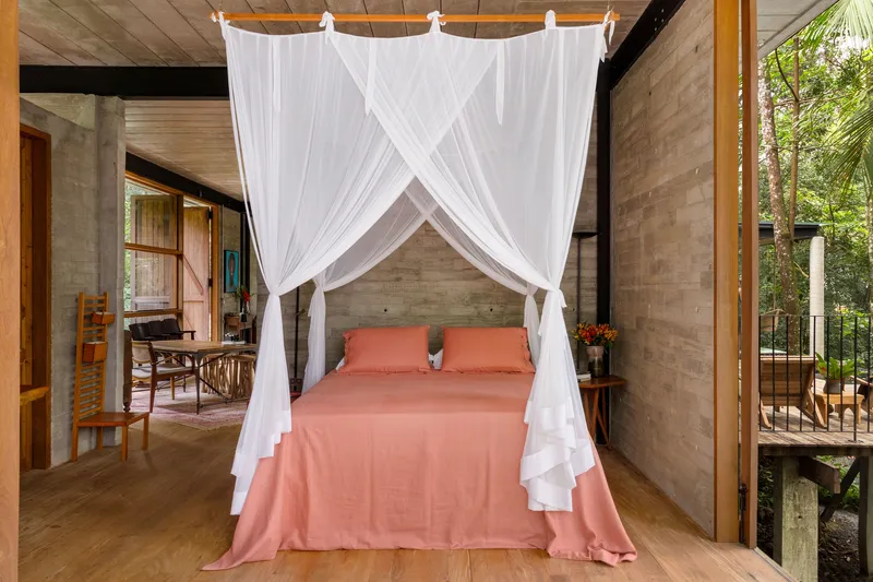 Bedroom with white canopy netting over bed and timber-planked ceiling opening to surrounding forest