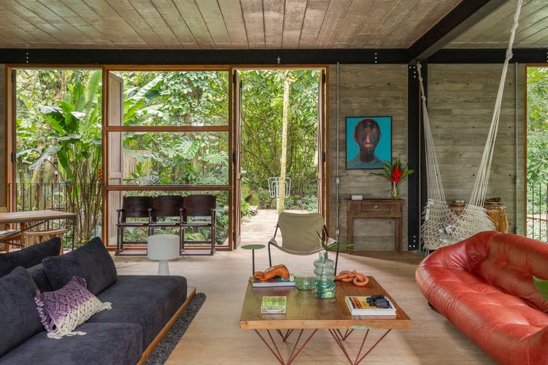 Living area with board-formed concrete walls and floor-to-ceiling windows framing tropical vegetation outside