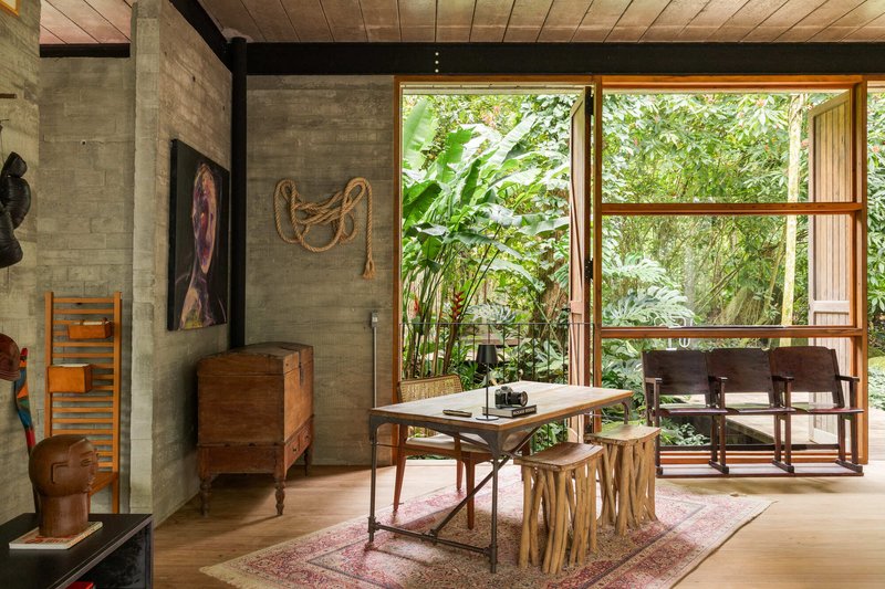 Dining space with timber table and concrete wall opening through glazed doors to lush garden beyond