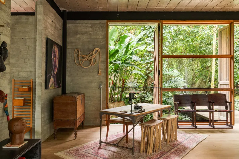 Dining space with timber table and concrete wall opening through glazed doors to lush garden beyond