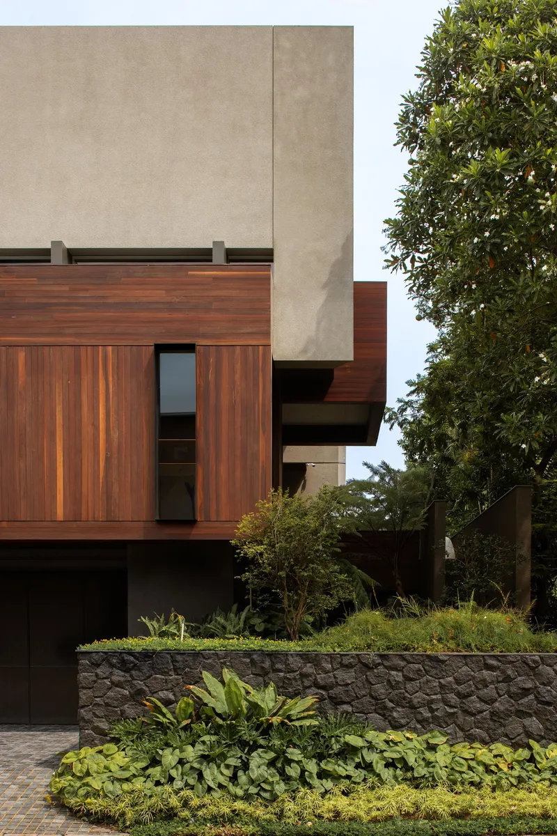 Facade detail showing vertical timber cladding and concrete panels framed by overhanging foliage
