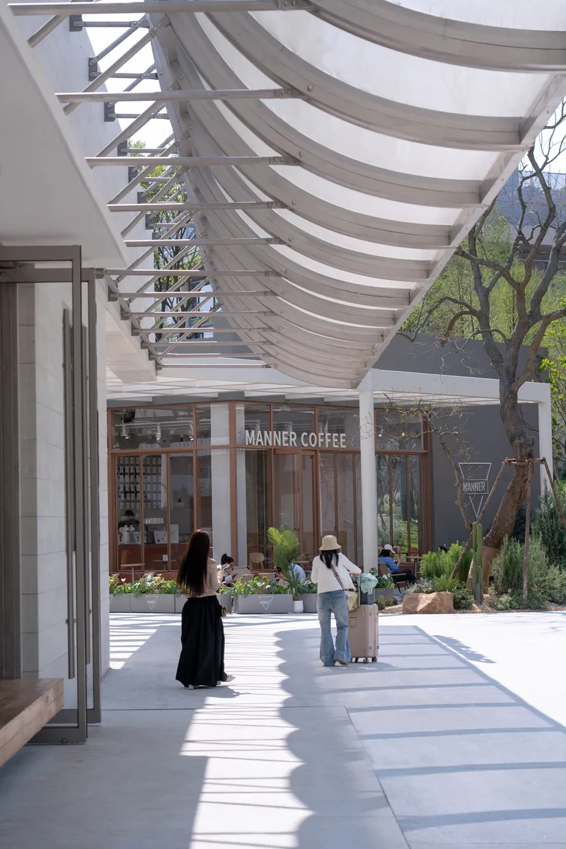 Covered walkway with undulating fabric canopy and steel framework casting shadows on pavement below