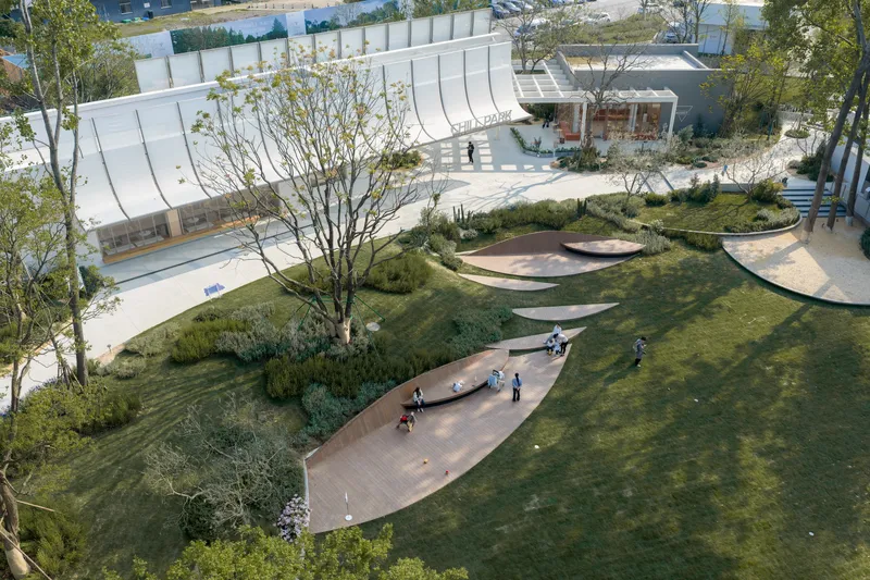 Aerial view of curving timber deck pathways threading through lawn and planted mounds with visitors