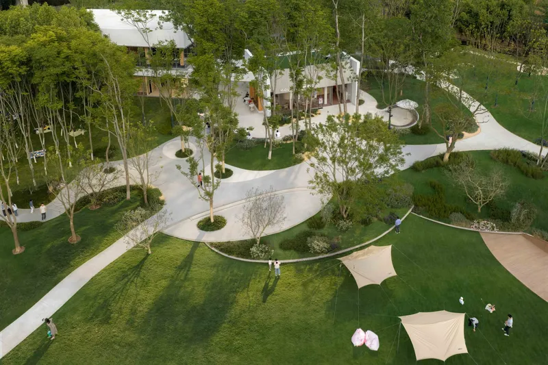 Overhead view of sinuous white concrete paths connecting lawn areas dotted with trees and shade structures