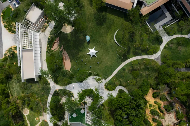 Overhead view of white star-shaped pavilion and meandering pathways through a green campus with trees