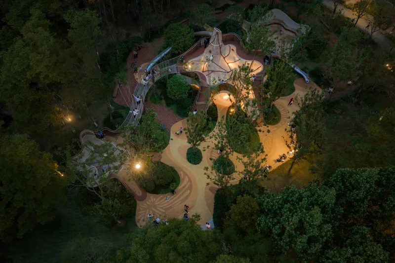 Aerial view at dusk of a curving playground structure with sand paths winding through trees